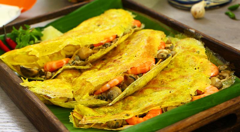 Đĩa gỏi cá trích Phú Quốc tươi ngon đầy màu sắc với cá, rau, dừa, hành tây, ớt bày trên lá chuối, cạnh chén nước chấm đậu phộng đặc trưng và bánh tráng cuốn.